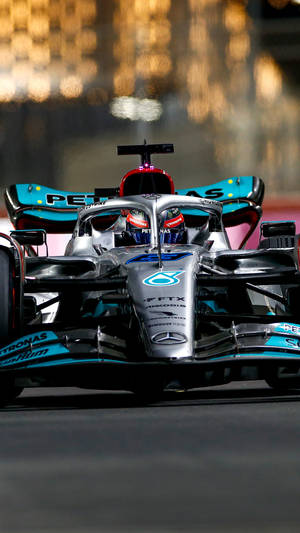 F1賽車在夜間賽道上高速行駛，背後有城市燈光。 — F1 iPhone 壁紙