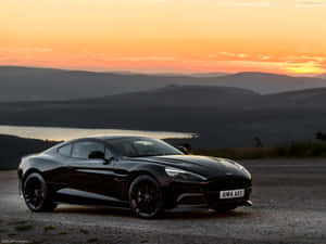 日落時分黑色 Aston Martin V12 Vantage 俯瞰群山和湖泊。 — 奧斯頓馬丁 壁紙