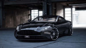 黑色Aston Martin跑車在昏暗的工業倉庫中，旁邊有混凝土地板和窗戶。 — 奧斯頓馬丁 壁紙
