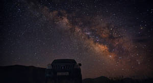 一輛汽車停泊在星空下，銀河清晰可見。 — 昏暗 壁紙