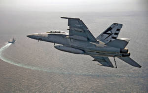 灰色戰鬥機在海洋上空飛行，下方軍艦留下白色航跡。 — 軍事動圖 壁紙
