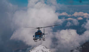 藍色直升機在積雪山峰附近的雲層上方飛行 — 直升機 壁紙
