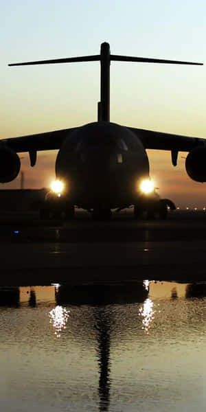 剪影軍用飛機，頭燈發光，在日落時反射在水坑中。 — 18:9 壁紙