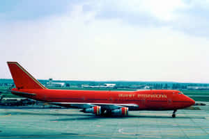機場停機坪上的紅色 Braniff International 波音 747，背景有機棚。 — MacBook Pro M3 壁紙