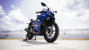 在多雲天空下的賽道上，藍色Yamaha R15運動機車立於支架上。 — 低飽和 壁紙