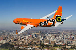 橙色Mango Airlines飛機在陽光明媚的日子飛越城市。 — 城市風景 壁紙