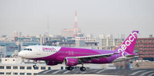 Peach Airlines飛機在城市景觀上空爬升，可見一座塔。 — 藍天 壁紙