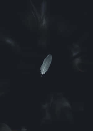 一根發光的白色羽毛懸浮在黑暗旋轉的煙霧中。 — 深色 iPhone 壁紙