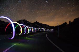 色彩繽紛的光圈沿著山路在繁星點點的夜空下延伸。 — 月亮與星星 壁紙
