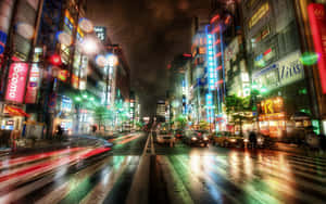 雨濕的東京街道，霓虹招牌和模糊的車燈在夜晚閃耀。 — 16:10 壁紙