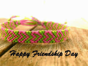 一條粉紅色和綠色編織友誼手環放在木頭上，帶有Happy Friendship Day文字。 — 友誼日 壁紙