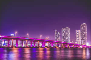 夜晚中，一座紫色燈光橋樑橫跨水面，背景是城市天際線。 — 邁阿密 壁紙