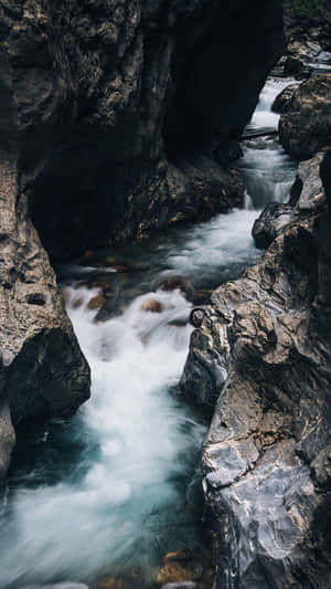 一條湍急的河流流經狹窄的岩石峽谷，峽谷壁呈深色。 — 白天 壁紙