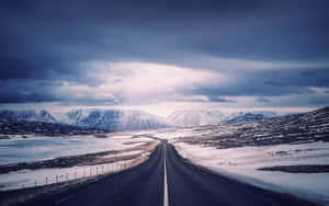 一條筆直的道路穿過雪地，遠處有山脈，天空多雲。 — 2880x1800 壁紙