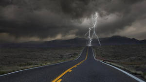一條直路在暴風雨下通往山脈，閃電劃破天空。 — 閃電 壁紙