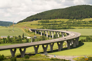 彎曲的混凝土高速公路橋橫跨綠色山丘，車輛行駛其中。 — MacBook Pro M4 壁紙