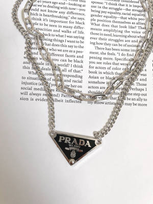 銀色 Prada 項鍊放在印有文字的打開書頁上 — 珠寶 壁紙