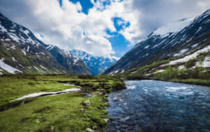 一條河流流經一個有雪山和藍天的綠色山谷。 — 河景 壁紙