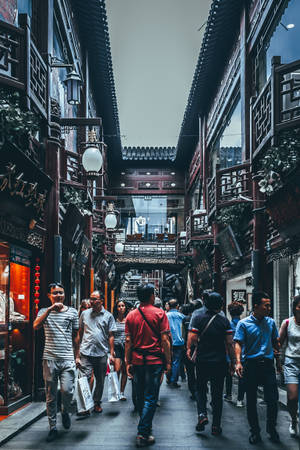 人們在狹窄的傳統中式小巷中漫步，兩旁有木製陽台和燈籠。 — 唐人街 壁紙