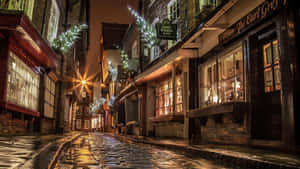夜晚狹窄的鵝卵石街道，節日燈飾和閃爍的商店櫥窗。 — 午夜 壁紙