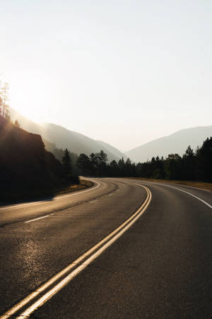 日出時穿過山脈的彎曲道路，兩旁是森林。 — 道路 壁紙