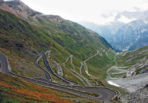 蜿蜒的山路，汽車在綠色和岩石地形上爬升。 — 山脈 壁紙