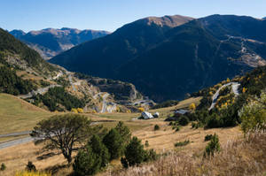 蜿蜒山路穿過秋日山谷，有樹木和遠處山峰。 — 山脈 壁紙