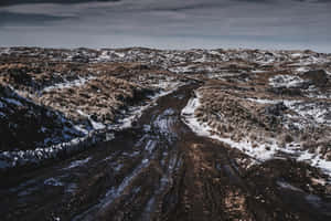 蜿蜒泥路穿過白雪覆蓋的山丘，天空多雲的冬季 — 冬季風景 壁紙