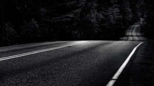 一條空蕩蕩的蜿蜒道路在黃昏時分消失在黑暗的森林中。 — 黑夜 壁紙