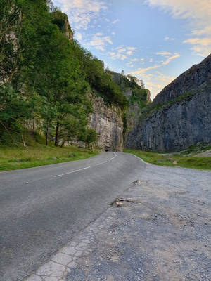 蜿蜒的道路穿過岩石峽谷，綠樹成蔭，藍天白雲 — 英國 壁紙