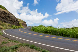 彎曲的道路穿過綠草和岩石懸崖，在藍天白雲下 — 山坡 壁紙