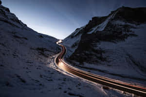 蜿蜒的積雪山路，黃昏時有汽車燈光軌跡。 — 冬季風景 壁紙