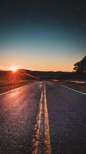一條道路在繁星點點的暮色天空下，地平線上有發光的太陽。 — 漂亮 iPhone 壁紙