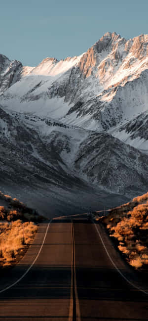一條通往日落時分雪山的道路。 — iPhone 15 Pro 壁紙