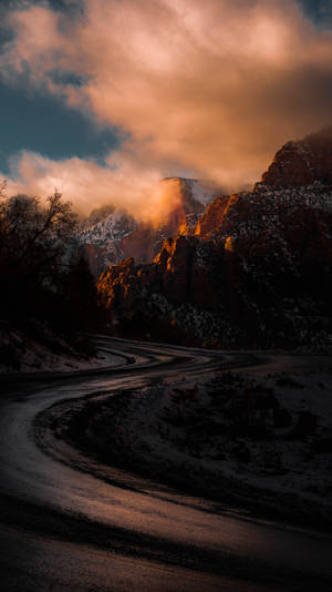 日落時分，金色光芒穿透雲層，照耀著蜿蜒的雪路穿過群山。 — 山坡 壁紙