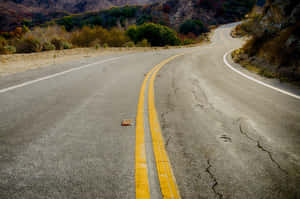 蜿蜒破裂的道路穿過乾燥的山丘，植被稀疏。 — 山坡 壁紙