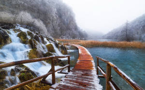 冬季中，被雪覆蓋的木棧道旁邊有流動的瀑布和藍色的湖泊。 — 克羅埃西亞 壁紙