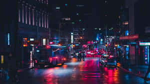 夜晚的城市街道，潮濕的路面反射著來自汽車和建築物的霓虹燈光。 — 城市燈光 壁紙