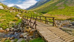 木橋橫跨山間溪流，綠丘藍天 — 木質紋理 壁紙