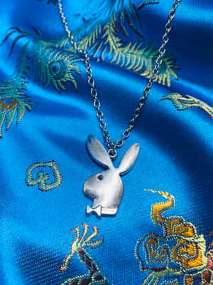 銀色Playboy兔子吊墜項鍊在藍色刺繡緞布上。 — iPad Pro 13 壁紙