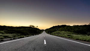 日落時分的空路，兩旁有綠色山丘。 — 道路 壁紙