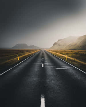 一條空蕩蕩的道路穿過草地平原，在灰色天空下伸向遠山。 — 山坡 壁紙