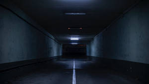 地下停車場中長而黑暗的混凝土隧道，帶有白色中線和閃爍的燈光。 — 暗黑地牢 壁紙