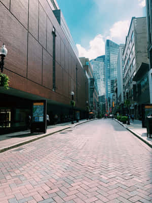 一條寧靜的都市街道，鋪有磚塊路面和高樓大廈，在晴朗的天空下。 — iPad Pro 12.9 壁紙
