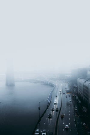 霧氣瀰漫的城市高速公路旁有水，遠處有建築物 — 下雨 壁紙