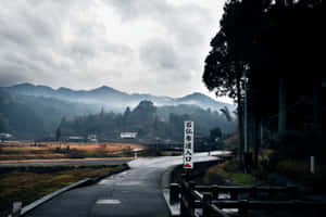 一條蜿蜒的道路穿過霧氣瀰漫的日本山脈，神社入口處有標誌。 — 日本 壁紙