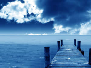 一條木碼頭在暴風雨的藍天下延伸到海洋。 — 海灘日落 壁紙