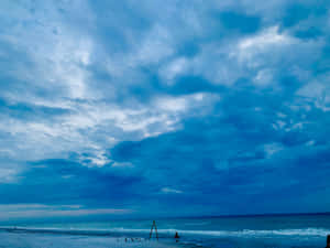 人們在沙灘上，背景是戲劇性的藍色多雲天空和海浪。 — 海灘日落 壁紙