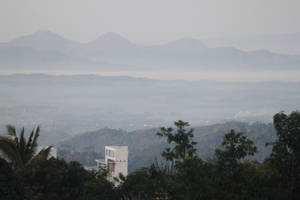 朦朧的山脈和山谷，前景有樹木和建築物 — 地形 壁紙