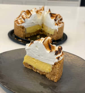 一片檸檬蛋白派，上面有烤過的配料，放在深色盤子上。 — Vivo X Fold3 壁紙